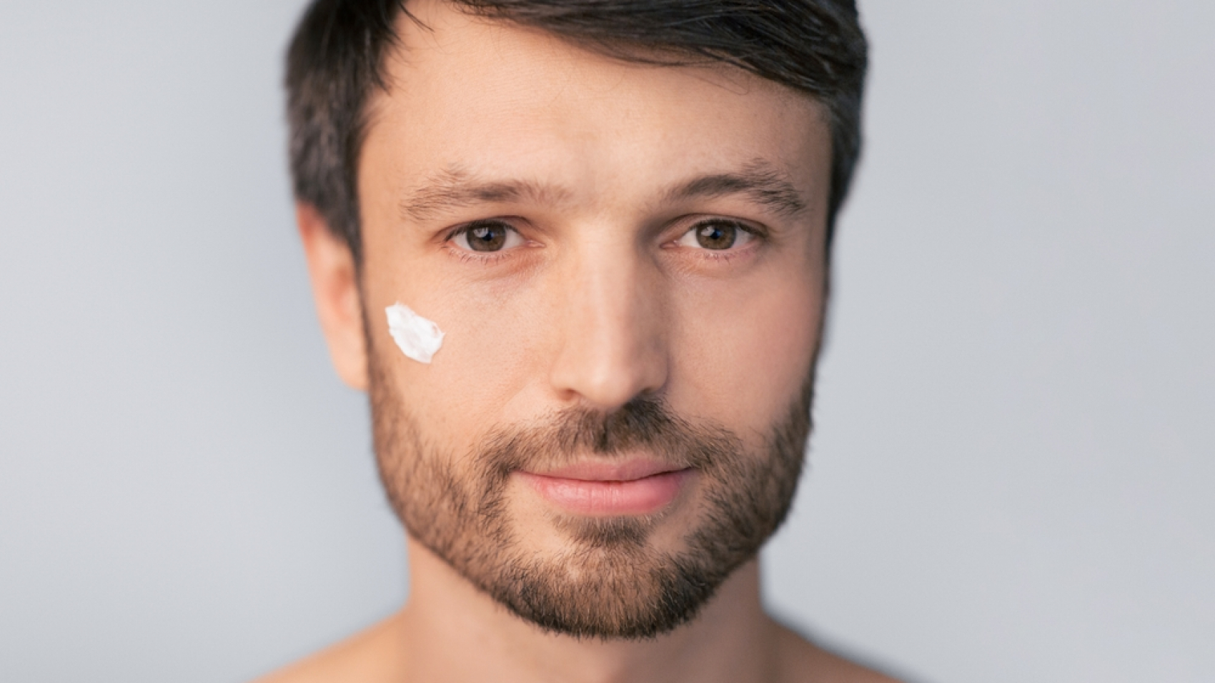 A,Man,With,A,Beard,Applies,Facial,Moisturizer,To,His